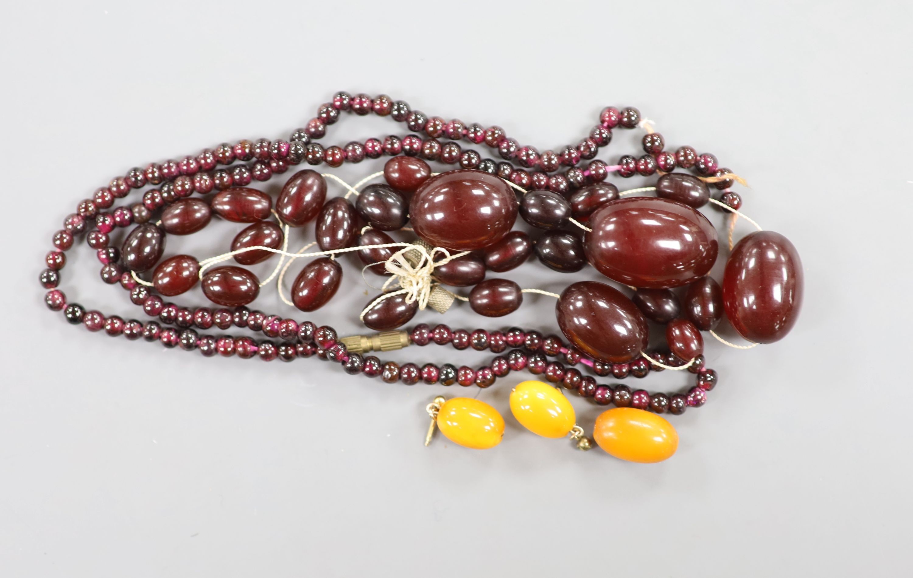 A pair of amber earrings, some loose simulated amber beads and a garnet bead necklace.